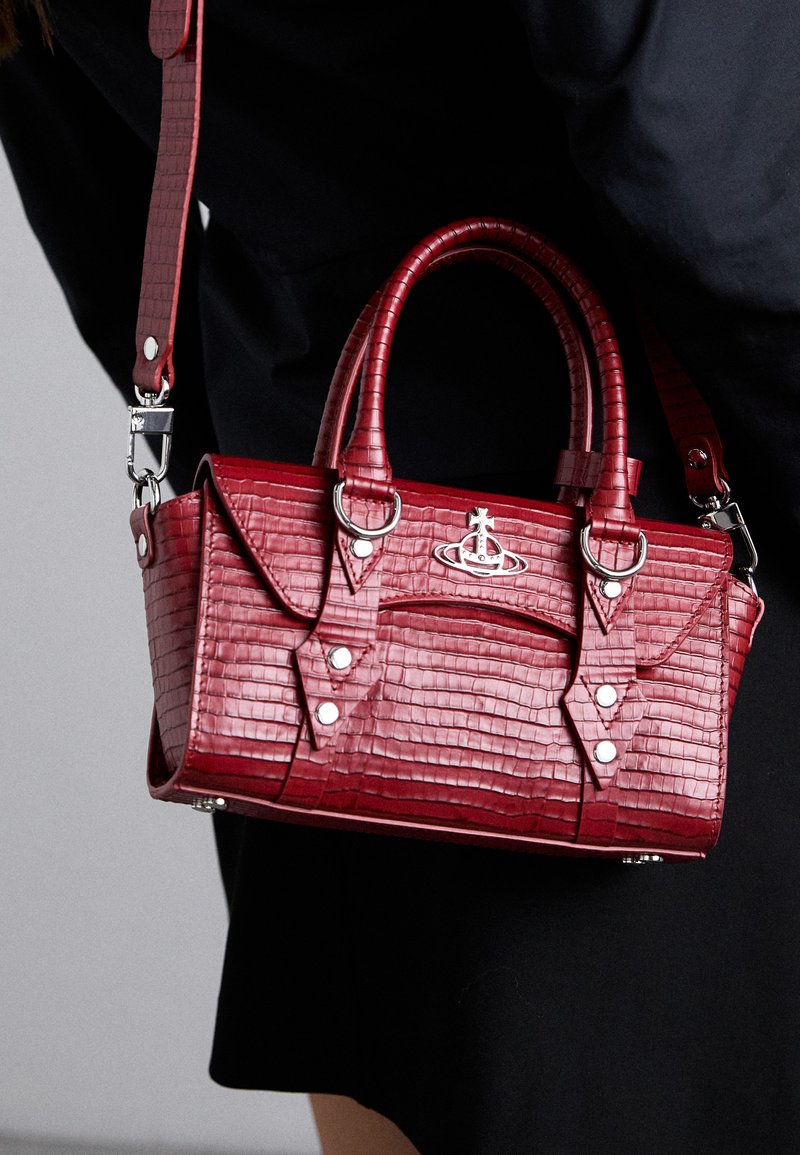 Red crocodile-patterned handbag with dual handles, detachable shoulder strap, metallic hardware, and structured design with snap details.