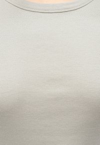 Svetlo siva zguban top z okroglim izrezom. Tkanina ima mehko teksturo in fine navpične proge po celotni površini.