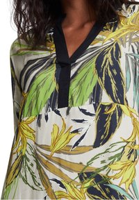 Chemise à motif floral en tissu léger, présentant des feuilles vertes et jaunes, un col noir et une coupe ample.
