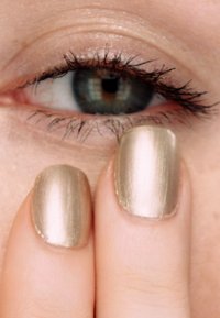 Metalliskt guld nagellack på fingrar, närbild av ett öga med blå iris och mörka fransar, som visar en slät hudtextur runt ögat.