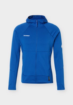 Mænds blå vindjakke med hætte, fuld lynlås, Mammut-logo på brystet, lynlåslommer og logo-patch på venstre ærme.