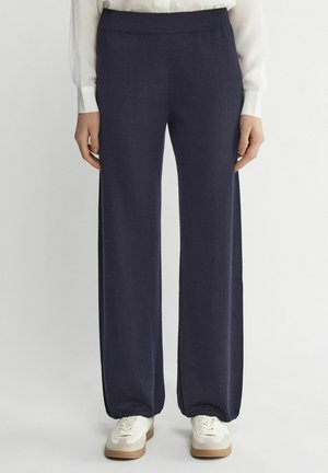 Marineblauwe wijde broek met een gladde textuur, elastische tailleband en minimale stikseldetails, gecombineerd met witte sneakers.