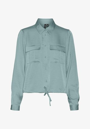 Blouse longue à manches longues en teal clair, en matière soyeuse, avec un devant à boutons, deux poches sur la poitrine et un détail à nouer au bord.