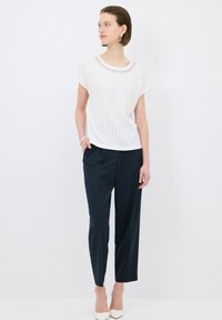 Top blanco de manga corta con patrón texturizado y escote joya, combinado con pantalones navy ajustados y tacones blancos de punta.