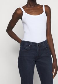 Witte geribbelde tanktop met vierkante halslijn, gecombineerd met donkere spijkerbroek. De stof is rekbaar; de jeans hebben standaard zakken en een knoopsluiting.