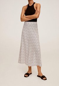 Sort ribbet tanktop parret med en hvid midi-nederdel med et sort plettet mønster. Modellen har sorte slidesandaler på. Glat stofstruktur.