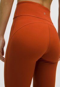 Oranje high-waisted leggings van rekbaar materiaal, met platte naden en een logo-detail bij de tailleband. Heeft een gladde textuur zonder patronen.
