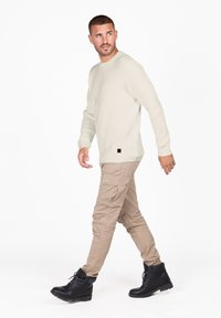 Hellbeige geripptes Sweatshirt kombiniert mit beigen Cargohosen und schwarzen Schnürstiefeln. Bemerkenswerte Texturen sind das Rippenmuster und die Cargotaschen.