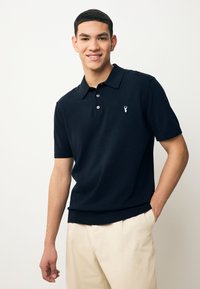 Marineblå kortærmet polo lavet af blødt stof, med ribstrikket krave og kant, samt en lille broderet hummertlogo på brystet.