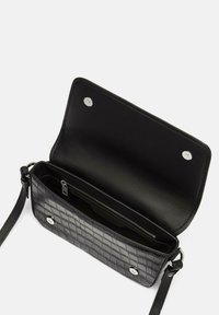 Sac en cuir noir à bandoulière avec une texture matelassée, quincaillerie en argent, poche intérieure zippée et fermeture à pression magnétique. Vue ouverte.