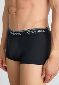 Zwarte boxershorts van een katoenmix met een dunne grijsgestreepte tailleband waarop het "Calvin Klein" logo in het wit staat. Aansluitend ontwerp, gladde textuur.