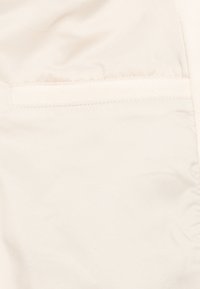 Lys beige stoff med en glatt tekstur og en skjult lomme. Sømmen er ren og pen, noe som bidrar til et strømlinjeformet design.