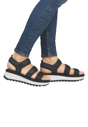 Black platform sandals with adjustable straps, textured material, and a thick white sole featuring a zigzag pattern. Suitable for casual wear.