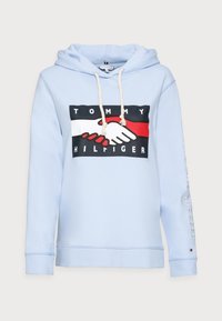Jasnoniebieska bluza z kapturem z graficznym nadrukiem splecionych rąk na przodzie oraz logo "Tommy Hilfiger", z beżowymi sznurkami i haftowanym tekstem na rękawie.