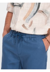 Pantalons à cordon de serrage bleus en tissu léger, offrant une coupe décontractée, des poches latérales et une texture lisse.