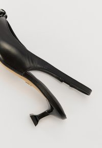 Črne usnjene črne čevlje na visokem petu s slingback obliko. Imajo sijoč peto in koničast nos, kar prikazuje gladko teksturo in minimalno šivanje.