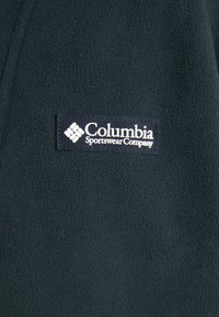 Tumed roheline fliiskangas tekstuuriga pinnaga. Omab sinist silti valge tekstiga: "Columbia Sportswear Company" ja logo.