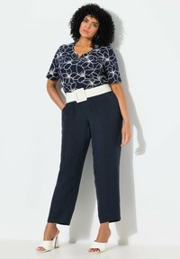 Marint blommig topp med V-ringning och korta ärmar, kombinerad med marint strukturerade byxor och ett brett vitt bälte. Vita öppna tå blockklackskor.