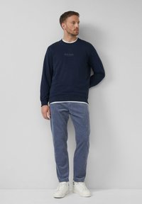 Marineblaues Sweatshirt mit Rundhalsausschnitt und gerippten Bündchen, kombiniert mit hellblauen Cordhosen und weißen Turnschuhen. Mit Logodetail auf der Brust.