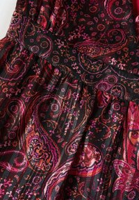 Tissu noir avec des motifs cachemire et floraux roses, violets et orange, avec des plis froncés et un détail de ceinture en tissu.