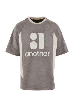 Tricou oversized gri cu o textură netedă, având text și forme grafice albe pe față și panouri laterale contrastante.