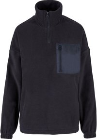 Pullover in pile nero con colletto alto e tasca frontale con zip. Presenta una texture morbida e polsini elastici per una vestibilità aderente.