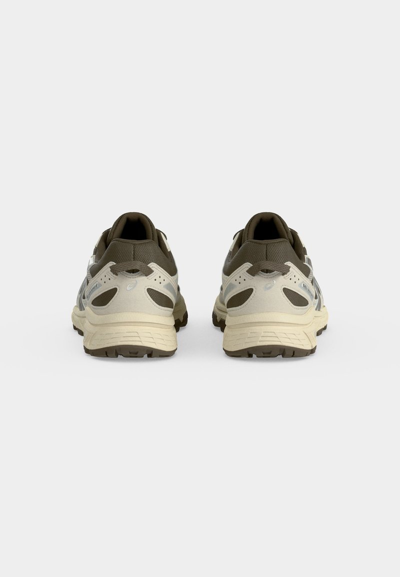 Par de zapatillas deportivas beige y marrón vistas desde atrás sobre un fondo blanco, mostrando detalles del talón y la suela.