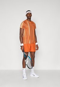 Tenis odijelo koje se sastoji od kratkih rukava narančaste pruge, odgovarajućih kratkih hlača i bijelih dodataka. Opremljeno teniskim reketom.