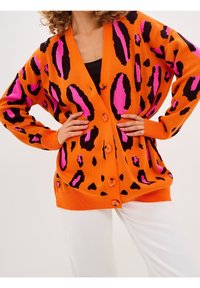 Oranger Cardigan mit einem schwarzen und pinken Leopardenmuster, mit Knopfleiste, gerippten Ärmeln und einem lässigen Schnitt.