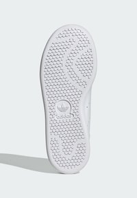 Άσπρη καουτσούκ σόλα αθλητικού παπουτσιού με υφές πρόσφυσης, που διαθέτει κεντρικό λογότυπο και στρογγυλεμένες άκρες για βελτιωμένη πρόσφυση.