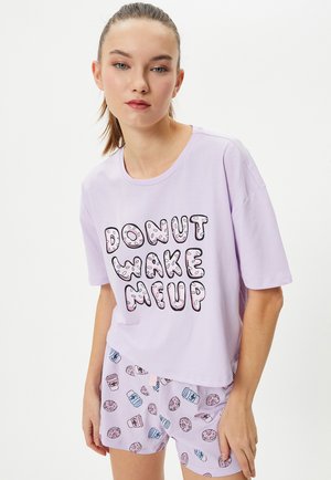 Lyse lilla bomulds t-shirt med teksten "DONUT WAKE ME UP"; parret med matchende shorts med donut- og kaffekop mønstre.