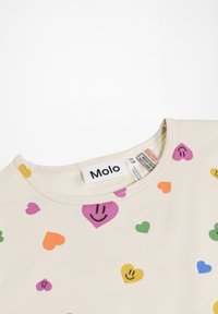 T-shirt beige chiaro con scollatura rotonda. Presenta stampe colorate di cuori e faccine sorridenti in rosa, verde, giallo, arancione e blu. Etichetta del marchio visibile.