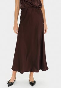 Gonna lunga in satin bordeaux con vita elasticizzata, caratterizzata da una forma fluida a trapezio e una texture liscia, abbinata a ballerine nere a punta.