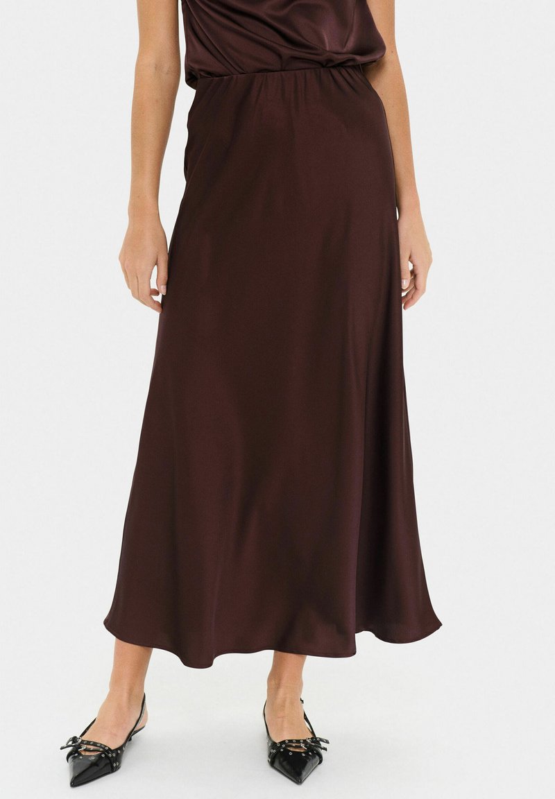 Gonna lunga in satin bordeaux con vita elasticizzata, caratterizzata da una forma fluida a trapezio e una texture liscia, abbinata a ballerine nere a punta.