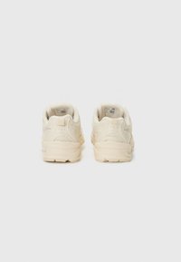 Beige treningsko med en teksturert mesh-overdel og glatt gummisåle. Har polstret krage og diskret logo-detalj på hælen.