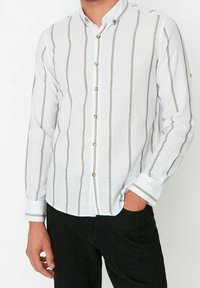 Valkoinen napitettava paita pystysuuntaisilla harmailla raidoilla, jossa koristeelliset kultaiset napit, pitkät hihat ja rento kauluksen muotoilu.
