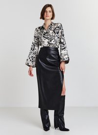 Black leather skirt with a side slit, paired with a floral print blouse in black and cream. Model wears knee-high black boots.