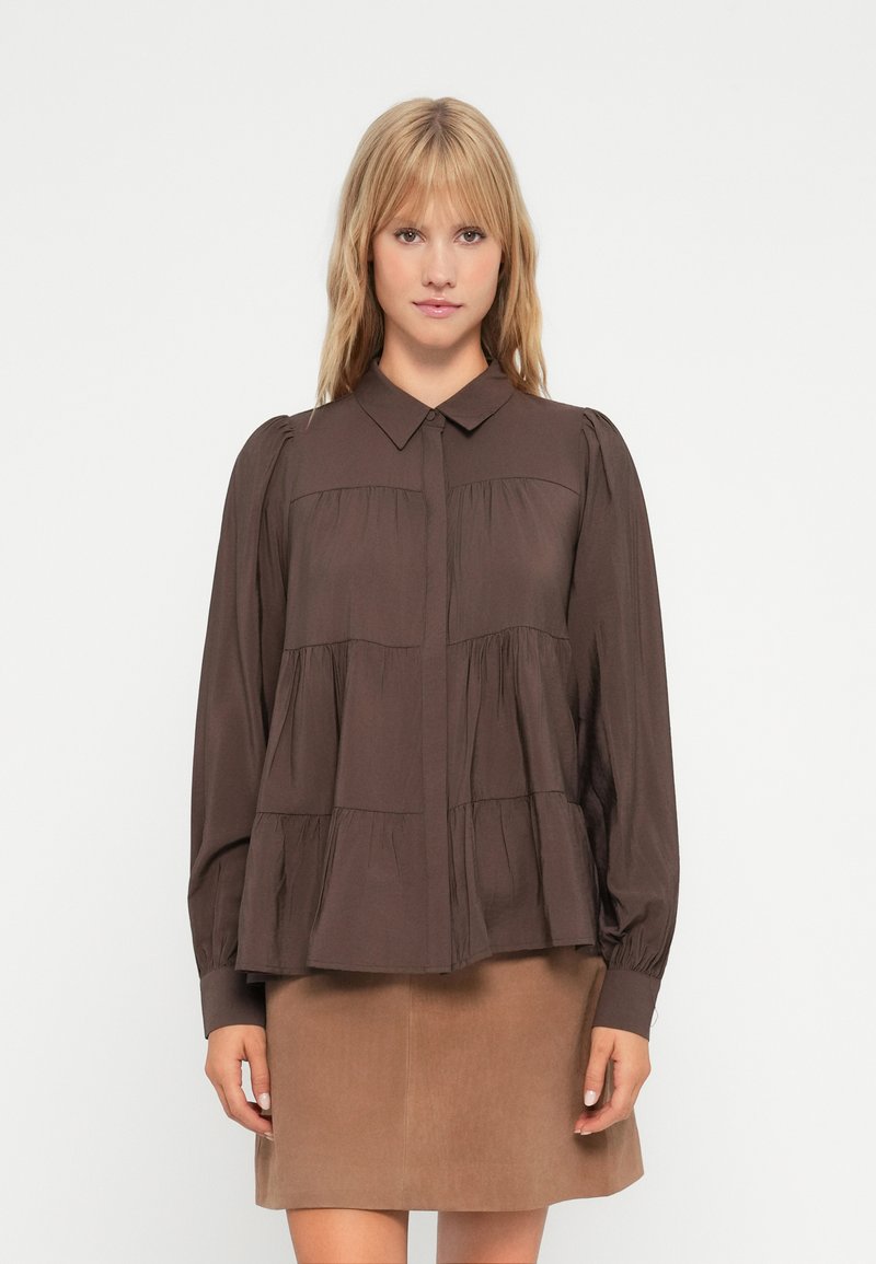 Brown long-sleeve blouse with a collared neckline, featuring a tiered design and gathered accents, paired with a tan skirt.