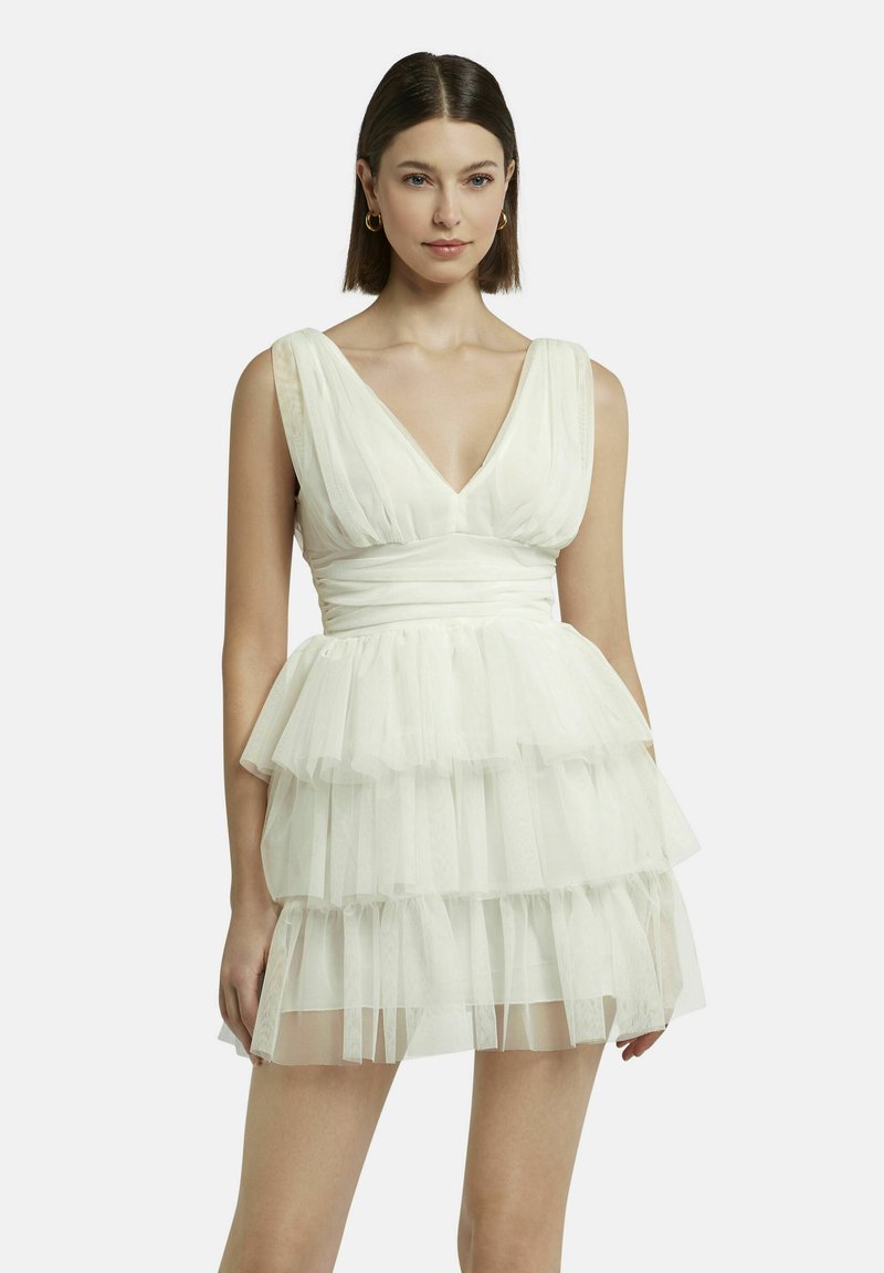 Robe en tulle blanche avec un décolleté en V, des bretelles épaisses, un corsage ajusté et une jupe à volants superposés. Le tissu translucide donne une texture légère et aérienne.