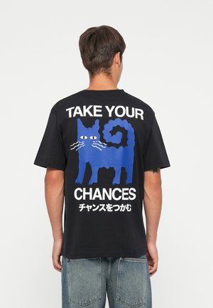 Black cotton t-shirt featuring a blue cat graphic with white text "TAKE YOUR CHANCES" and Japanese characters on the back. Short sleeves, relaxed fit.