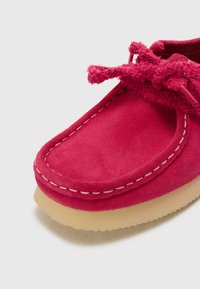 Scarpa in suede di un vivace colore rosa con un accento legato sul davanti, cuciture a contrasto e una suola in gomma beige con una finitura testurizzata.