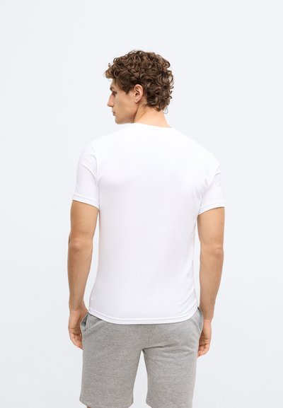 Balta kokvilnas T-krekls ar apaļu kakla izgriezumu, īsām piedurknēm un pieguļošu dizainu, kopā ar pelēkiem šortiem. Drēbes aizmugures skats.