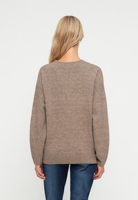 Brun strikkegenser med rund hals, avslappet passform, senkede skuldre og ribbestrikket kant. Myk tekstur, ingen synlige mønstre eller detaljer.