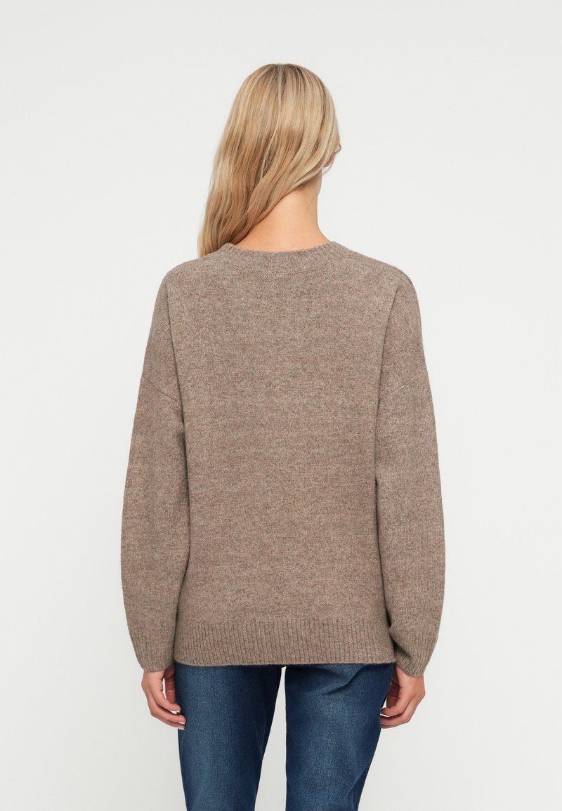 Brązowy dzianinowy sweter z okrągłym dekoltem, luźnym krojem, z opadającymi ramionami i żebrowanym dołem. Miękka tekstura, brak widocznych wzorów lub akcentów.