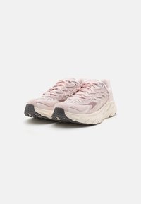 Zapatillas deportivas de color rosa claro con parte superior de malla texturizada, cierre de cordones resistente y una entresuela gruesa de color crema, con una suela exterior de goma negra.