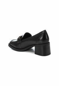 Zapatos de cuero negro con tacón cuadrado, con punta redonda y herrajes decorativos en la parte delantera. Textura suave y diseño limpio.