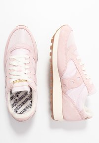 Une paire de baskets Saucony roses avec des lacets blancs, des semelles intermédiaires beige et des semelles extérieures en caoutchouc couleur gomme, présentée en vue de dessus et de côté.