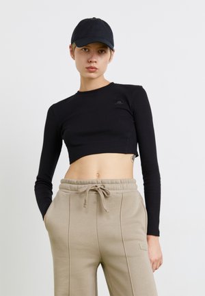 Crni rebrasti crop top s dugim rukavima i malim logom na prsima, u kombinaciji s bež duksericama koje imaju elastičnu traku u struku i bočne džepove.