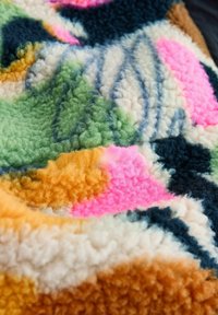Textured, colorful fabric featuring abstract patterns in green, pink, orange, navy, and cream. Soft, plush looped fibers for warmth.