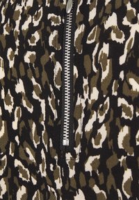 Tessuto in stampa leopardata nero e marrone con una cerniera argento visibile e rifiniture nere, caratterizzato da una superficie testurizzata e un motivo astratto.